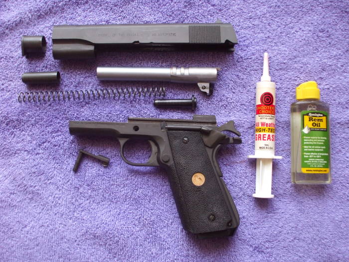 Parkerized M1911 pistol parts ready for lubrication and reassembly.  Red 'all weather high-tech' grease and a small bottle of 'Rem Oil' containing teflon.