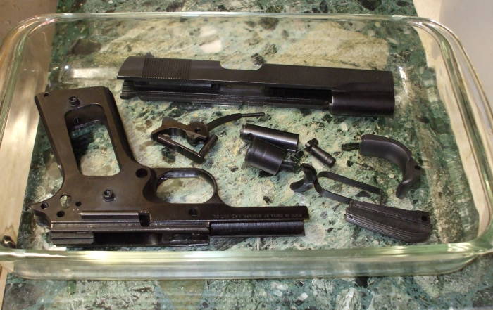 Bluing removal, removing bluing from gun parts with a vinegar bath.  The parts are in a glass dish and covered with vinegar.