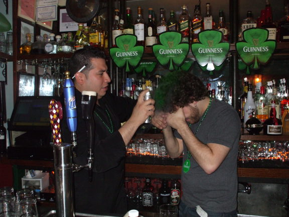 One bartender spraying the other's hair green.